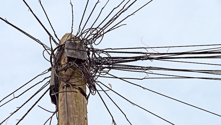 Image of a power pole with disorganized wiring structures referencing complexity